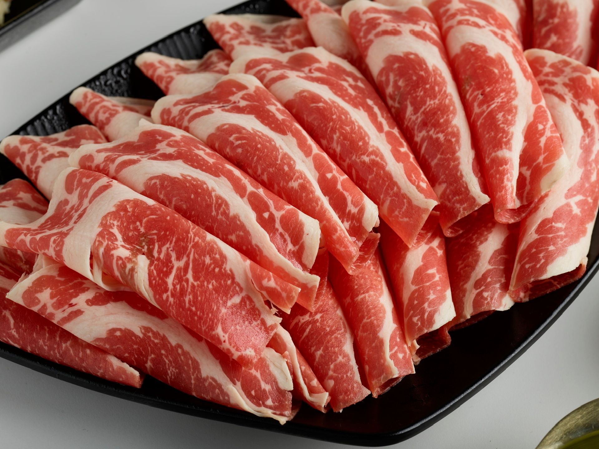 Close-up of thinly sliced raw beef arranged on a black plate, showcasing marbled patterns.