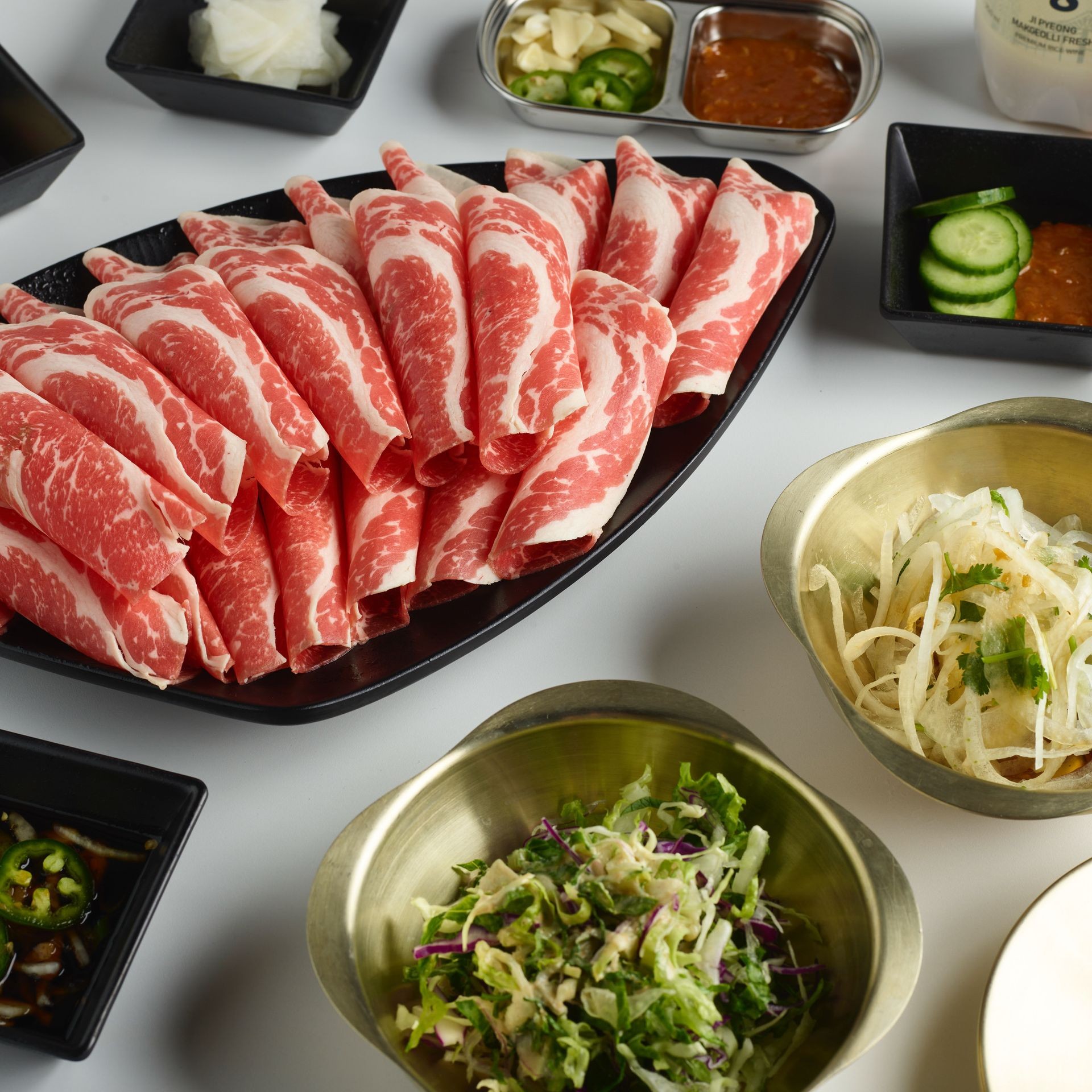 Platter of sliced raw beef with side dishes of vegetables and sauces on a table.