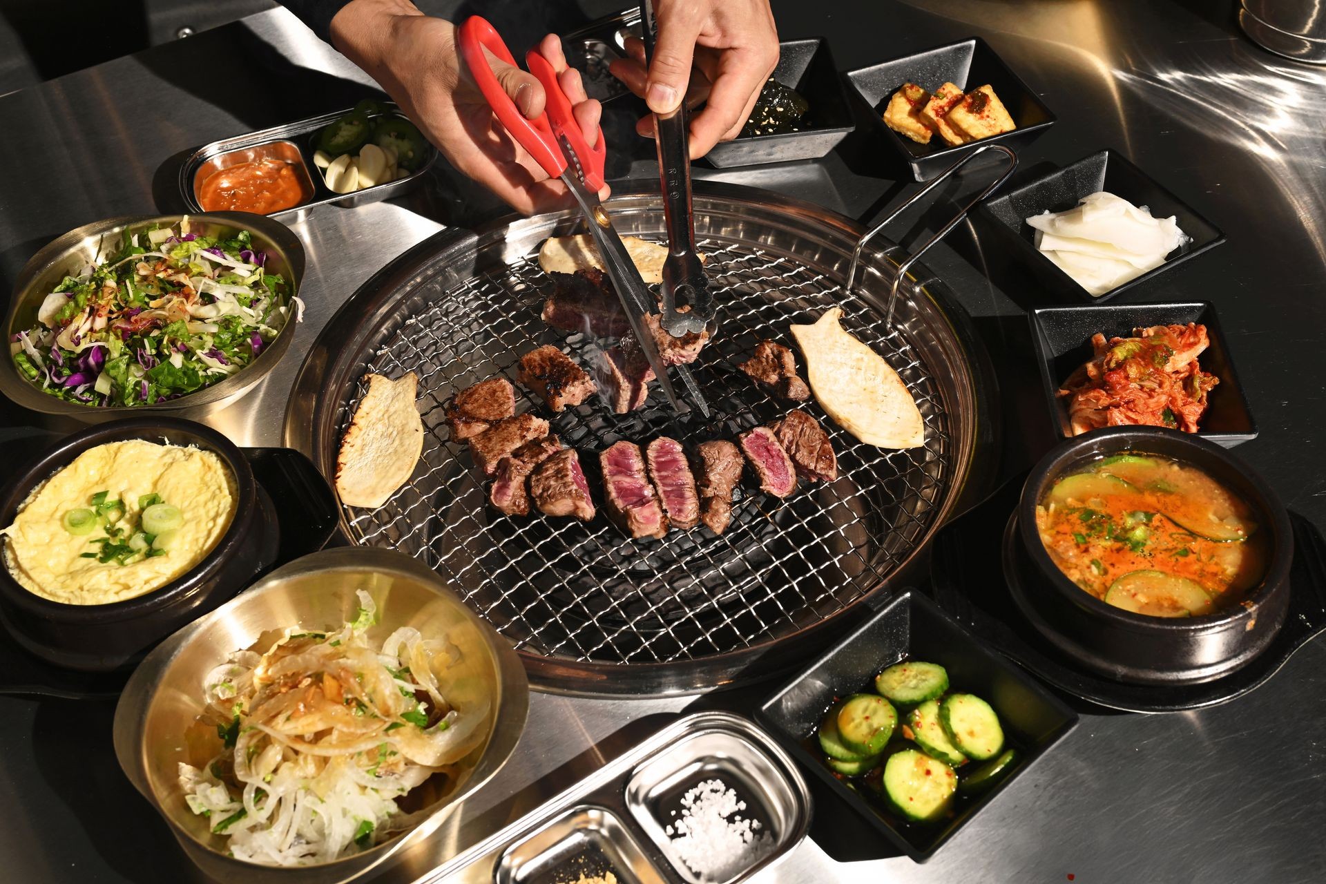 Korean barbecue with grilled meat, side dishes, and sauces on a metal grill table.