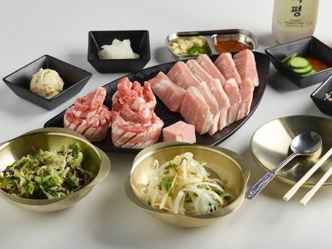 Assorted Korean BBQ meats and side dishes arranged on a table with chopsticks and a spoon.