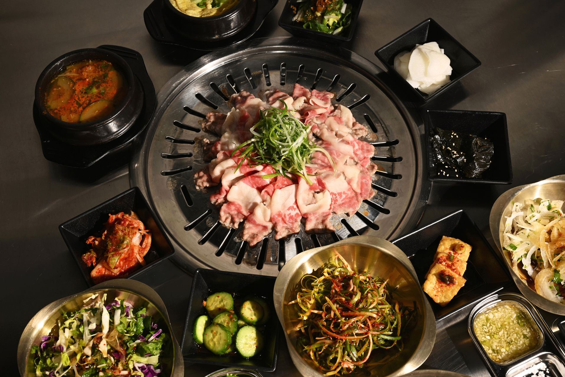 Korean BBQ setup with grilled meat on a table surrounded by various side dishes in bowls.