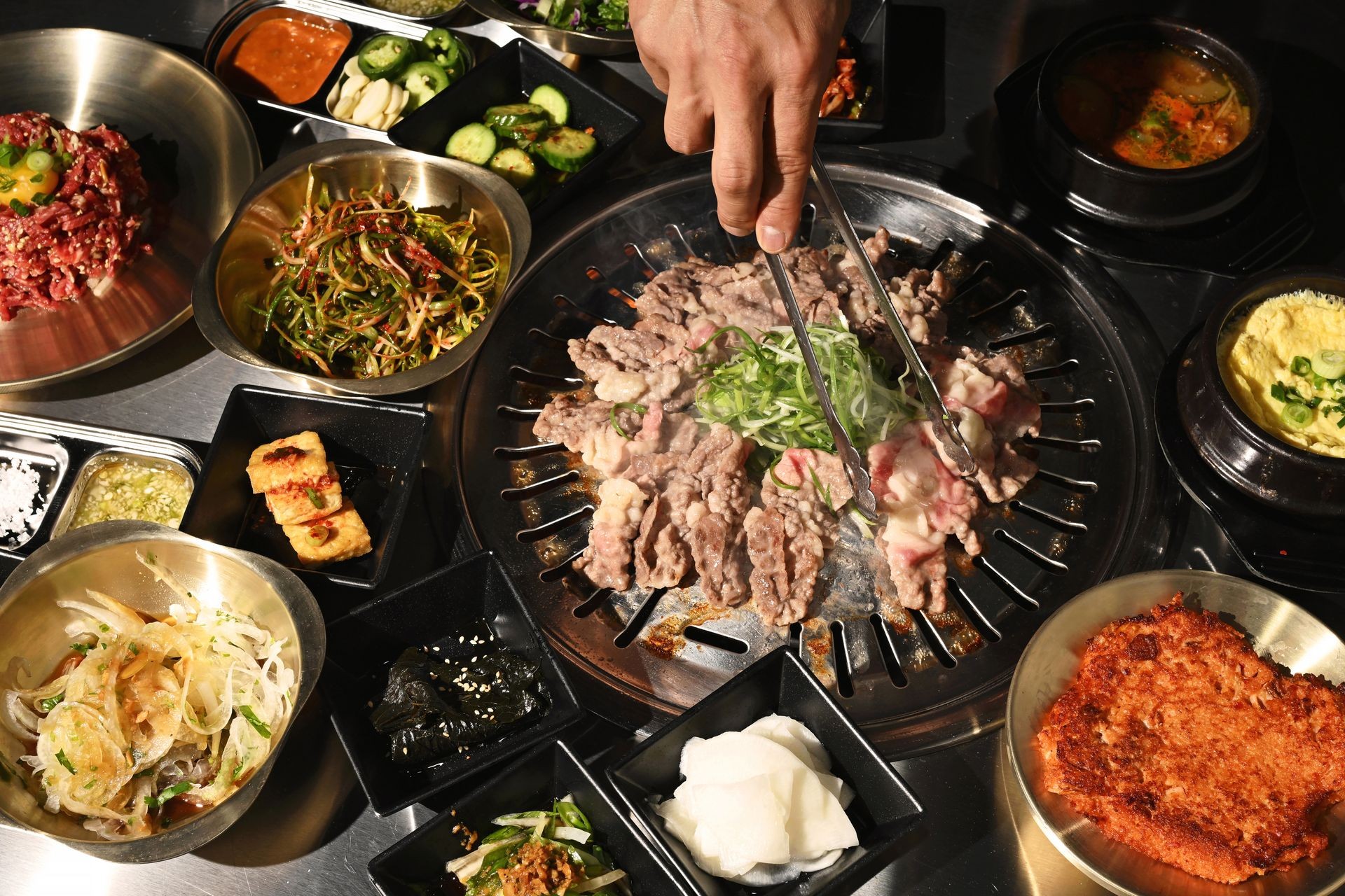 Korean BBQ meal with grilled meat, side dishes, and dipping sauces on a table.