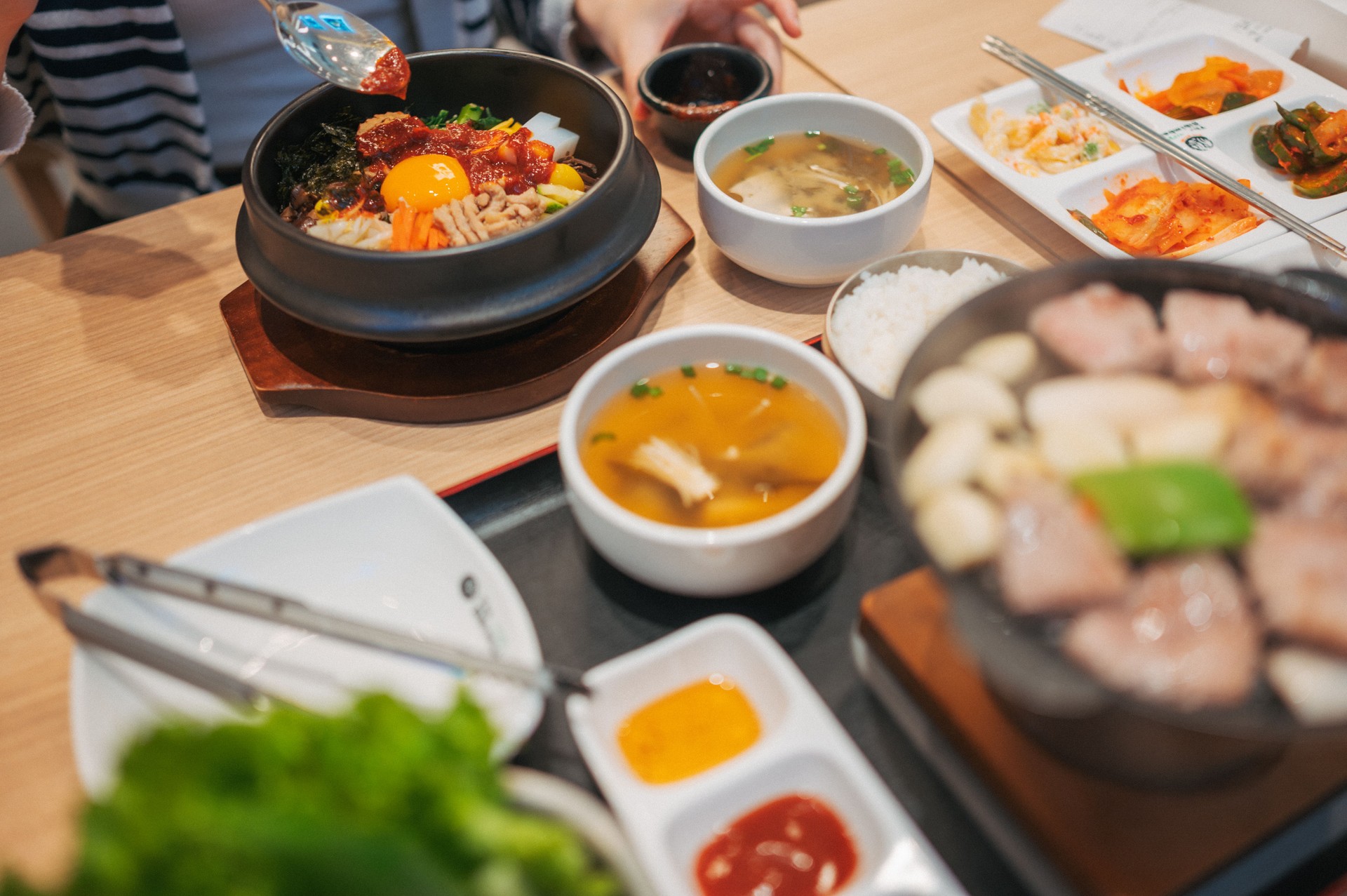 Top-down view of korean bibimbap with served alongside traditional korean side dishes  and hot plate pork korean BBQ with 3 style of sauce