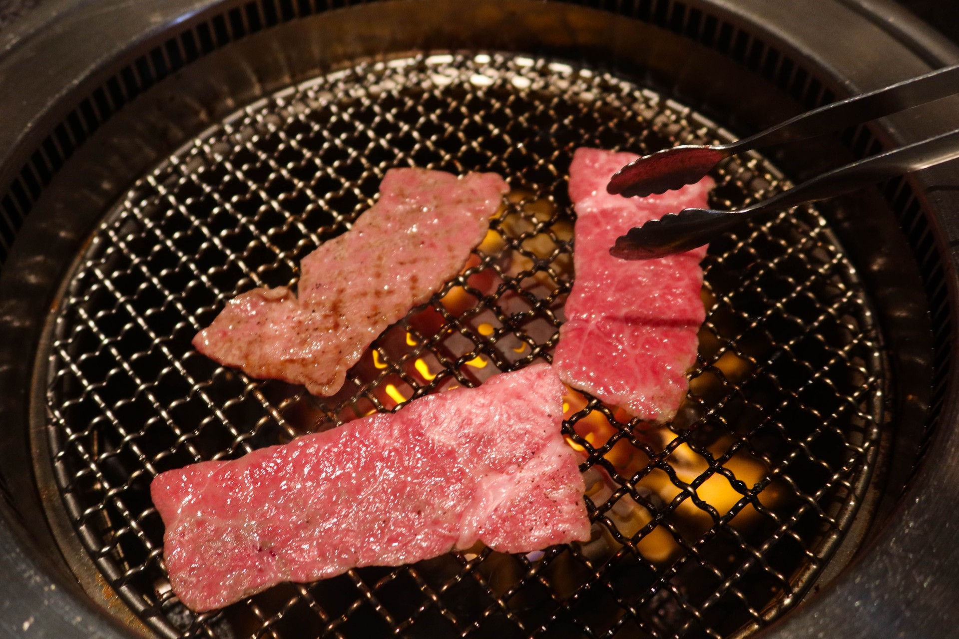 close up of three pieces of yakiniku grilled Japanese wagyu beef with charcoal fire in the stove with a clip  grilling the meat